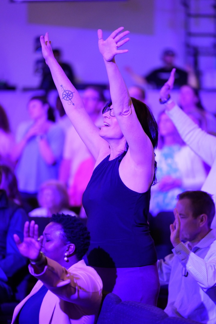 Woman worshipping with hands raised, purple stage lighting
